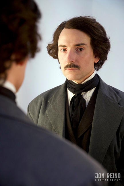 Campbell Harmon as Edgar Allan Poe, looking at the viewer from a mirror reflection. In the extreme foreground is the back of his head and shoulder.